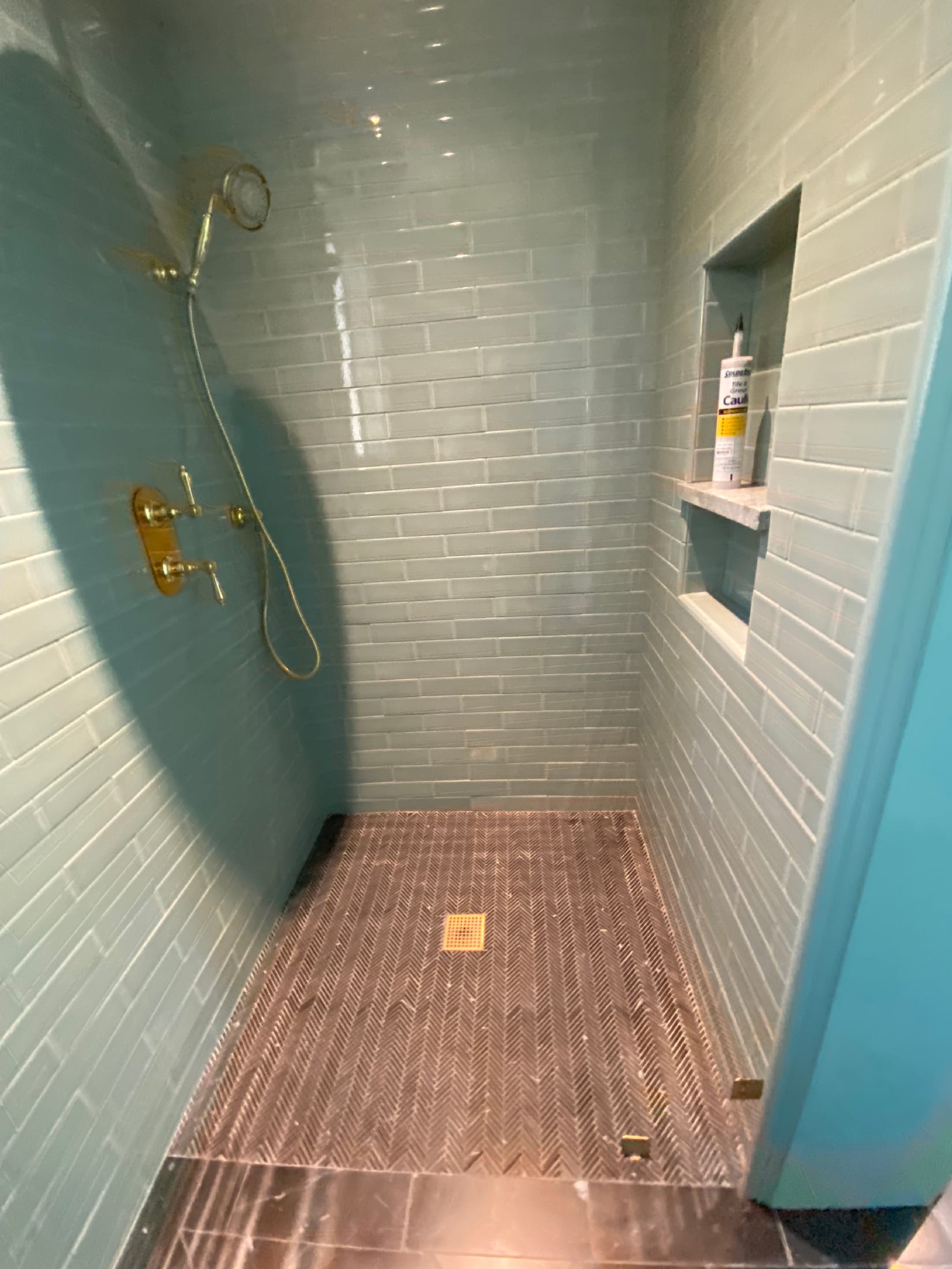 Walk-in shower in soft blue glass subway tile with a herringbone marble pan and a recessed niche.