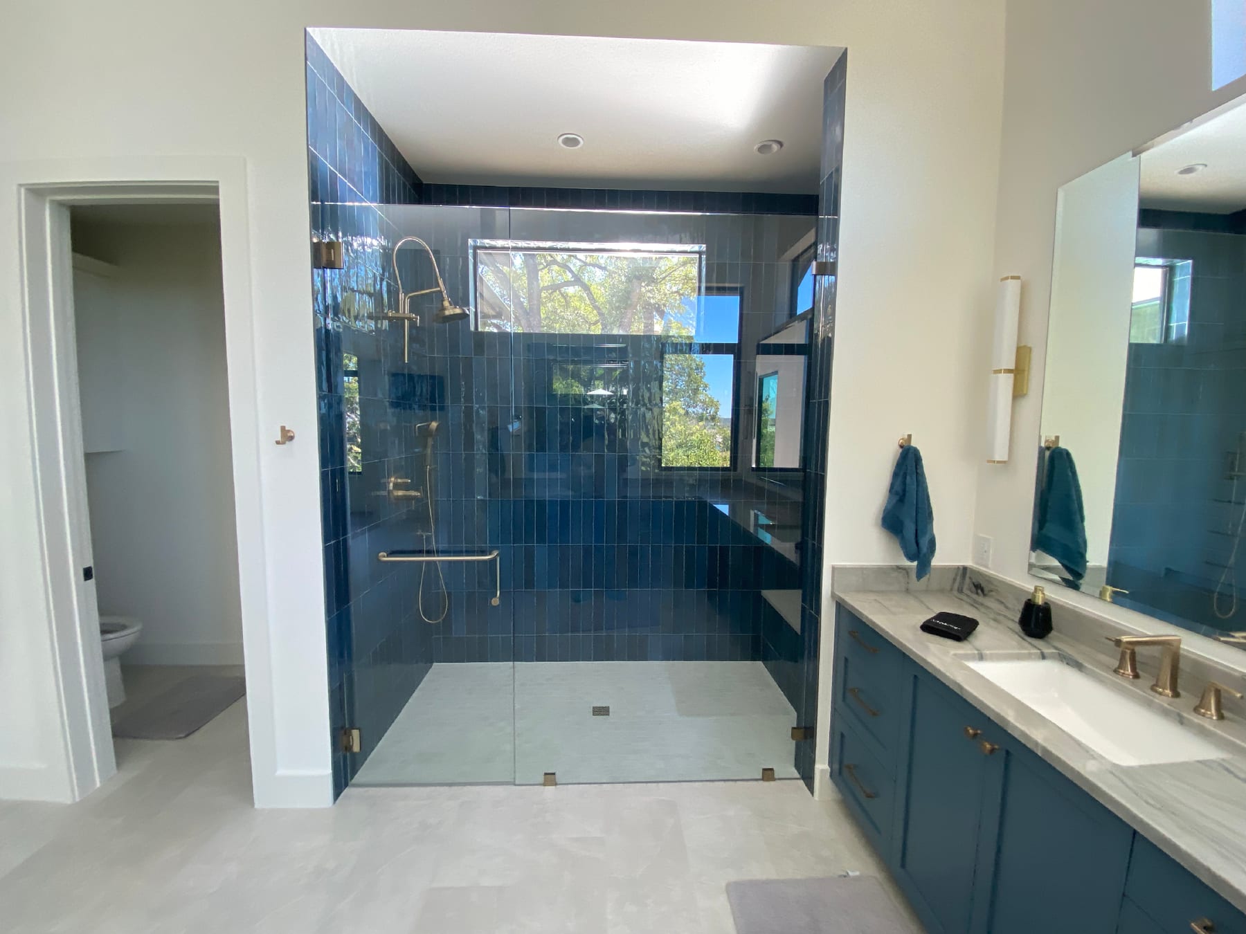 Wide walk-in shower with navy stacked tile walls, brass fittings, and a frameless glass door, set against a custom navy vanity.